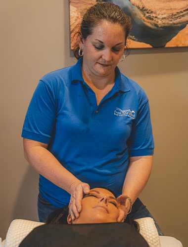 A therapist provides a facial massage to a client, promoting relaxation and wellness in a tranquil spa setting. The therapist wears a blue shirt with a logo.